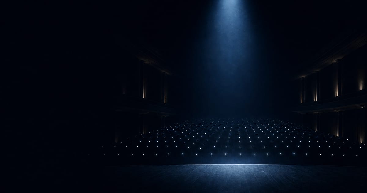 A dark theater viewed from the stage with a blue spotlight over the audience